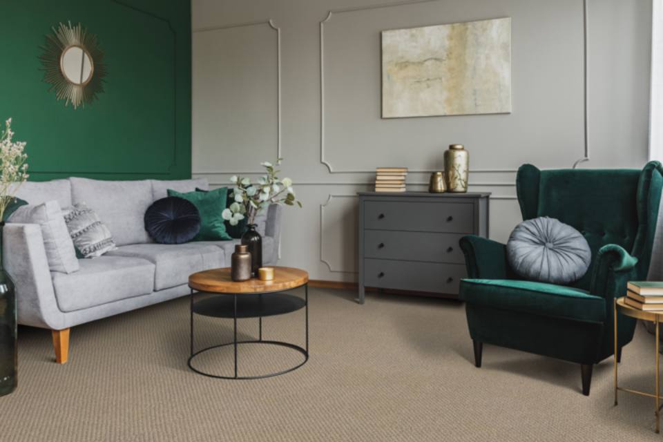 Green accent chair in living room with grey couch and tan carpet.